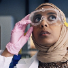 amina in lab gear, adjusting her goggles and looking around in confusion